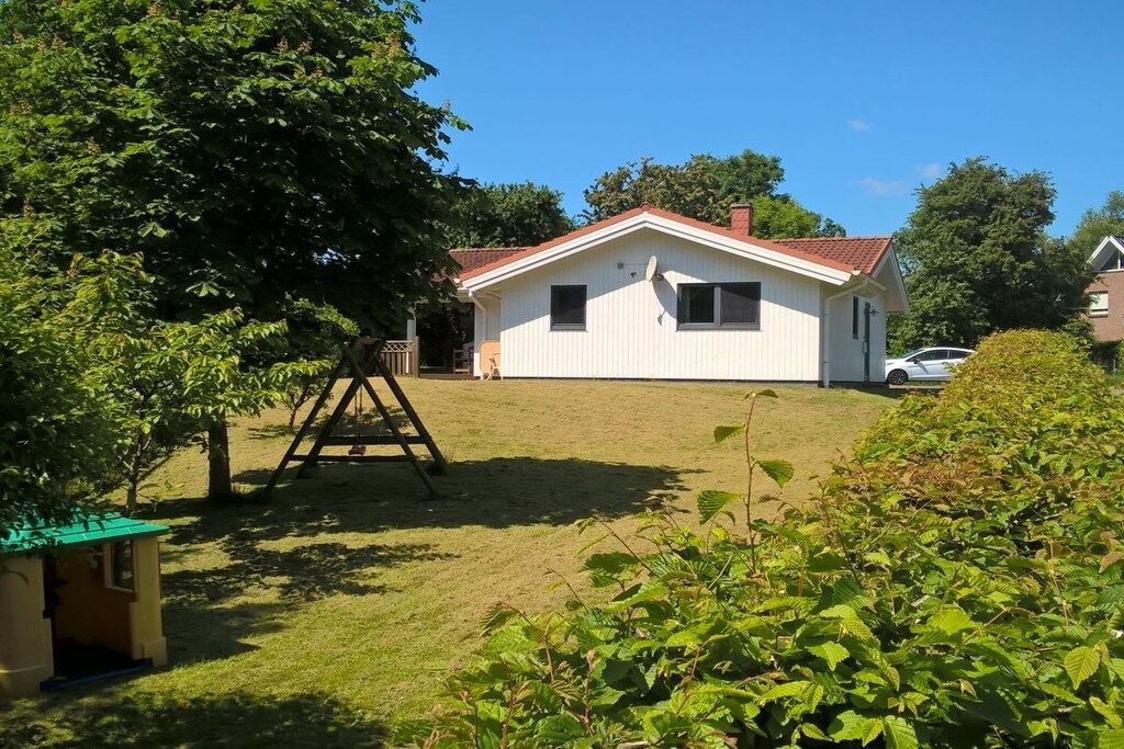 A single-story house with a red roof, a small porch, and a swing set in the yard.
