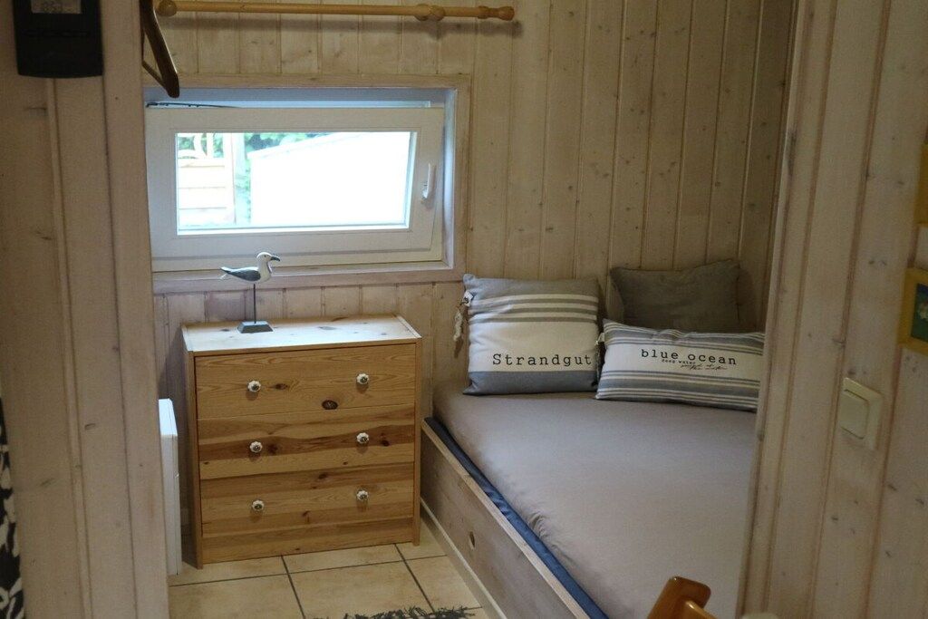 A wooden room with a bed, a dresser, a window, and a small table.