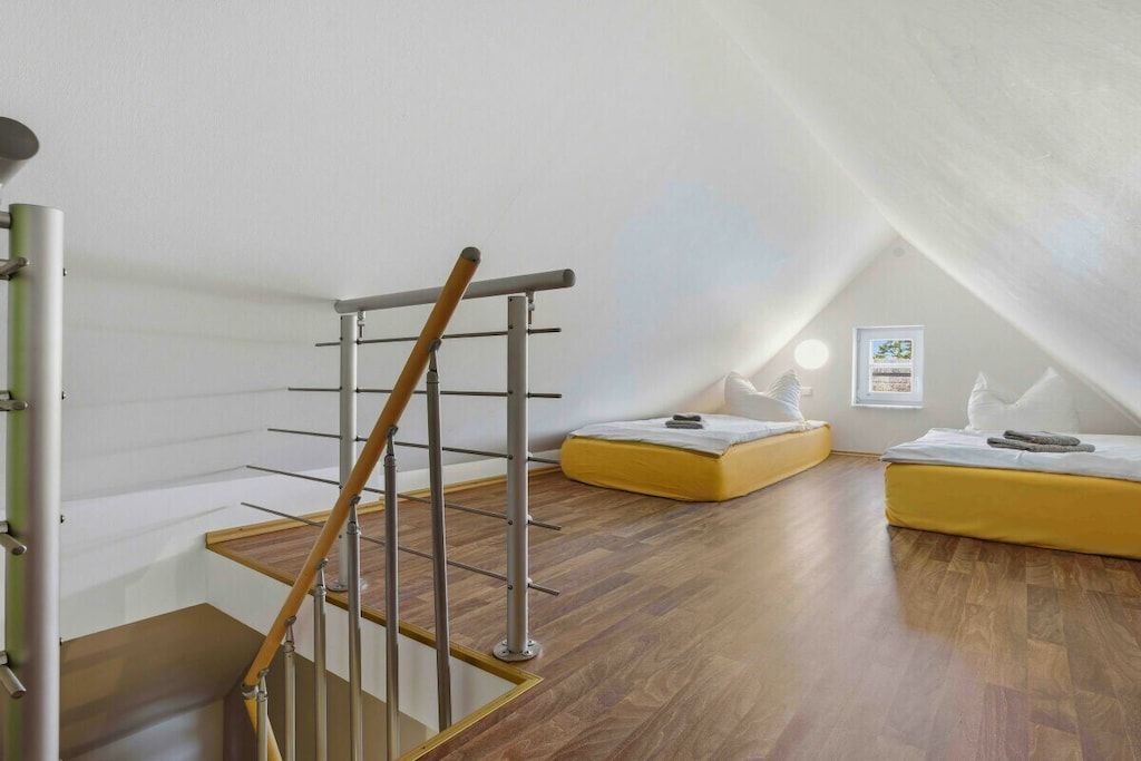 Habitació amb una escala de fusta, un sofà groc i una paret blanca amb un quadre encadrejat.