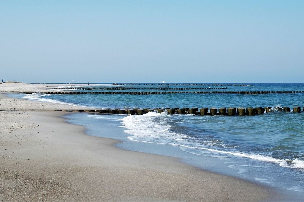 Een strand met een houten steiger en een heldere lucht.