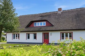 Ein traditionelles Haus mit einem Strohdach, einer roten Tür und nummerierten Fenstern.