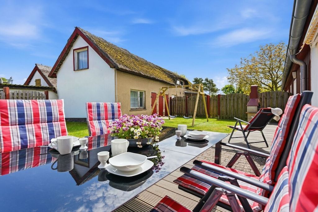Eine Terrasse mit Esstisch, Sitzgelegenheiten im Freien und einem Haus mit einem Strohdach im Hintergrund.