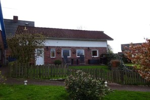 A two-story house with a brick facade, a front porch with chairs, and a wooden fence. - Holiday home with 2 bedrooms (Krautsand)