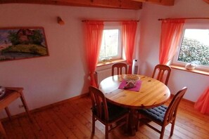 A dining area with a wooden table and chairs, a radiator, and a window with curtains. - Holiday home with 2 bedrooms (Krautsand)