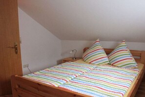 A single bed with a striped blanket, two pillows, a bedside table with a lamp, and a wooden headboard. - Holiday home with 2 bedrooms (Krautsand)