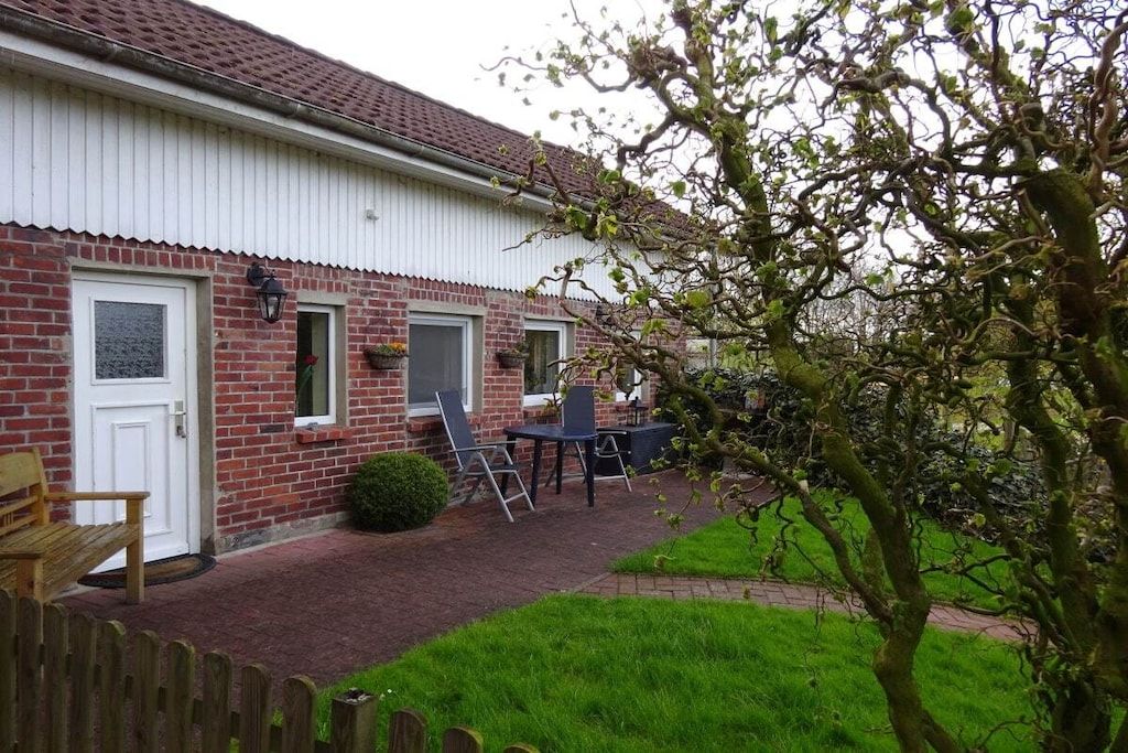 Une maison en briques avec une porte blanche, un petit patio avec une table et des chaises, et une clôture en bois.