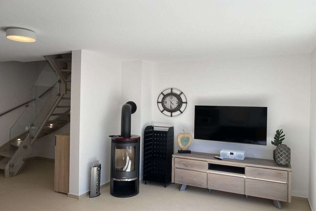 A modern living room with a fireplace, a flat-screen TV, a clock, and a staircase.