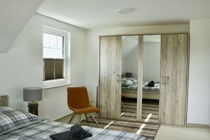 A bedroom with a bed, a chair, a wardrobe, and a window. - Holiday home with 2 bedrooms (Ostseeheilbad Zingst)
