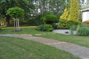 A garden with a paved walkway, a wooden arbor, and various shrubs and trees. - Altschulze "Panorama" (Schwielochsee OT Zaue)