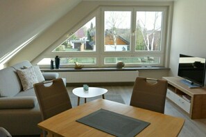 A modern living room with a sloped ceiling, a sofa, a dining table, and a television. - Altschulze "Panorama" (Schwielochsee OT Zaue)