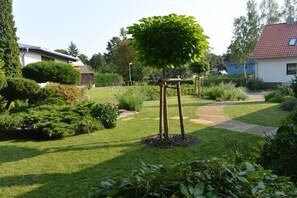 A well-maintained garden with a central tree, surrounded by neatly trimmed hedges and a variety of shrubs. - Altschulze "Panorama" (Schwielochsee OT Zaue)