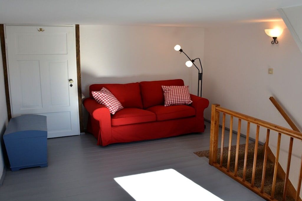 A room with a red sofa, a blue cabinet, a white door, and a staircase with a wooden railing.