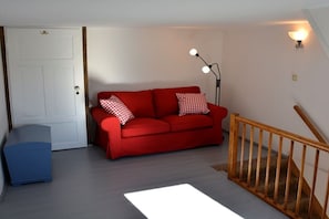Une pièce avec un canapé rouge, une armoire bleue, une porte blanche et un escalier doté d’une rampe en bois.