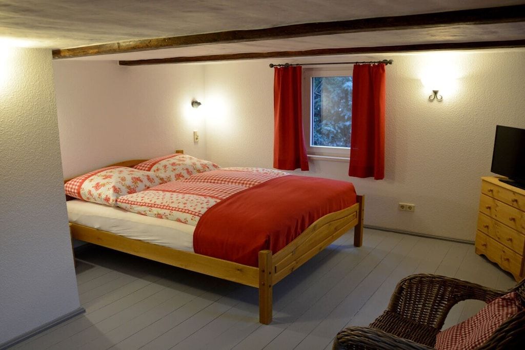 Ein Schlafzimmer mit einem hölzernen Bett, einem Nachttisch, einem Fernseher und einem Fenster mit Vorhängen.