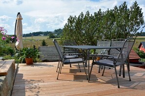 Eine Terrasse mit Gartenmöbeln, darunter ein Tisch und Stühle, umgeben von Topfpflanzen und mit Blick auf eine Landschaft mit Bäumen und einer entfernten Aussicht.