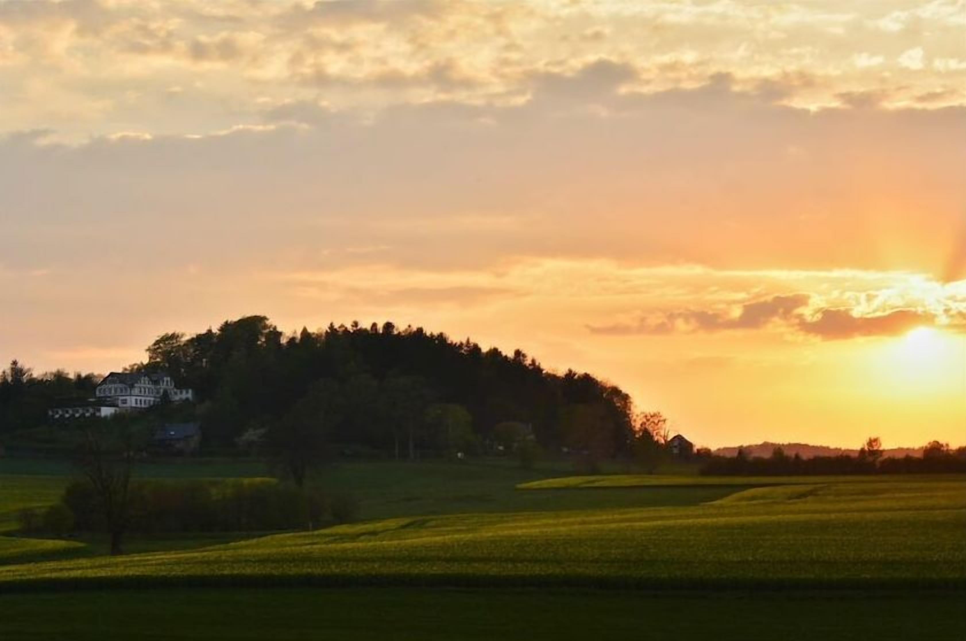 A sunset over a rural landscape with a house on a hill.