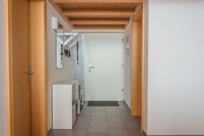 Un corridoio stretto con soffitto in legno, una porta bianca in fondo e un mobile bianco con cassetti a sinistra.