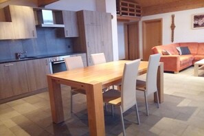 Eine moderne Küche mit Holzschränken, einem Esstisch mit Stühlen und einem Wohnbereich mit Sofa und einem Gemälde an der Wand.