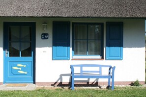Un bâtiment avec un toit de chaume, une porte bleue ornée de motifs de poissons découpés, et un banc à l’extérieur.