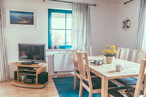 A room with a TV, wooden furniture, a window, and a wall-mounted life preserver. - Holiday home with 3 bedrooms (Wieck a. Darß)