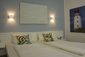 A hotel room with a bed, two wall-mounted light fixtures, a painting of a lighthouse, and a bedside table with a vase. - in the sea view apartment in Binz (Binz)