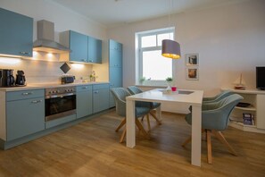 A modern kitchen with light blue cabinets, a white dining table, and a large window providing natural light. - in the sea view apartment in Binz (Binz)