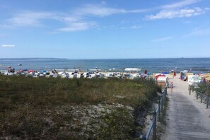 A beach with a boardwalk leading to the water, lined with beach umbrellas and chairs. - in the sea view apartment in Binz (Binz)