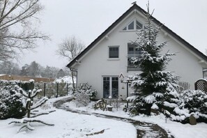 Une maison à deux étages avec un jardin enneigé et un chemin bien visible menant à l’entrée.