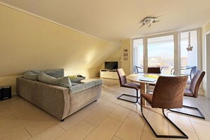 Un salon moderne avec un canapé, une table à manger et des chaises, un téléviseur et un balcon avec vue.