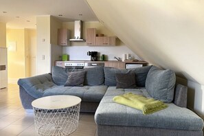 A modern living room with a sectional sofa, a round coffee table, and a kitchen in the background. - Holiday apartment Strandloper (Zinnowitz)
