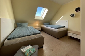 A small, triangular room with two beds, a skylight, and a nightstand with a lamp. - Holiday apartment Strandloper (Zinnowitz)
