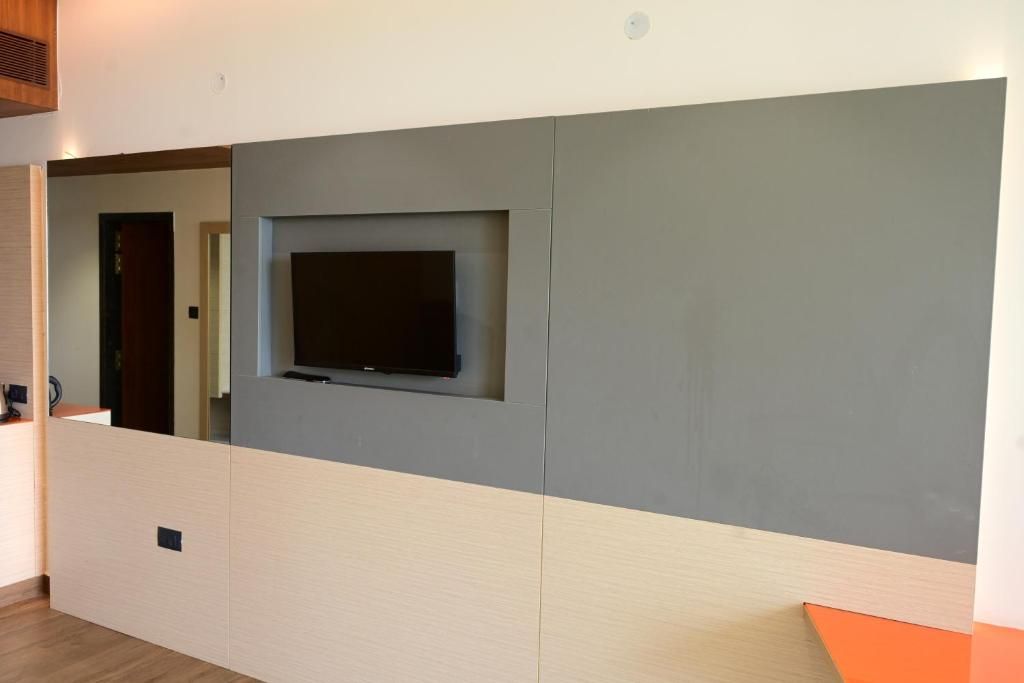 Une pièce avec un téléviseur encastré dans un mur gris, un plancher en bois et une vue partielle sur une porte.