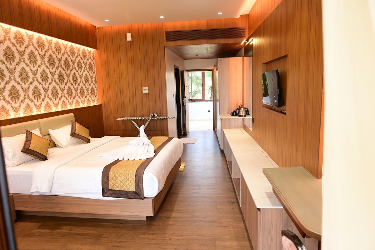 Habitación de hotel con una cama grande, una mesita de noche, un televisor en la pared y vistas al exterior.