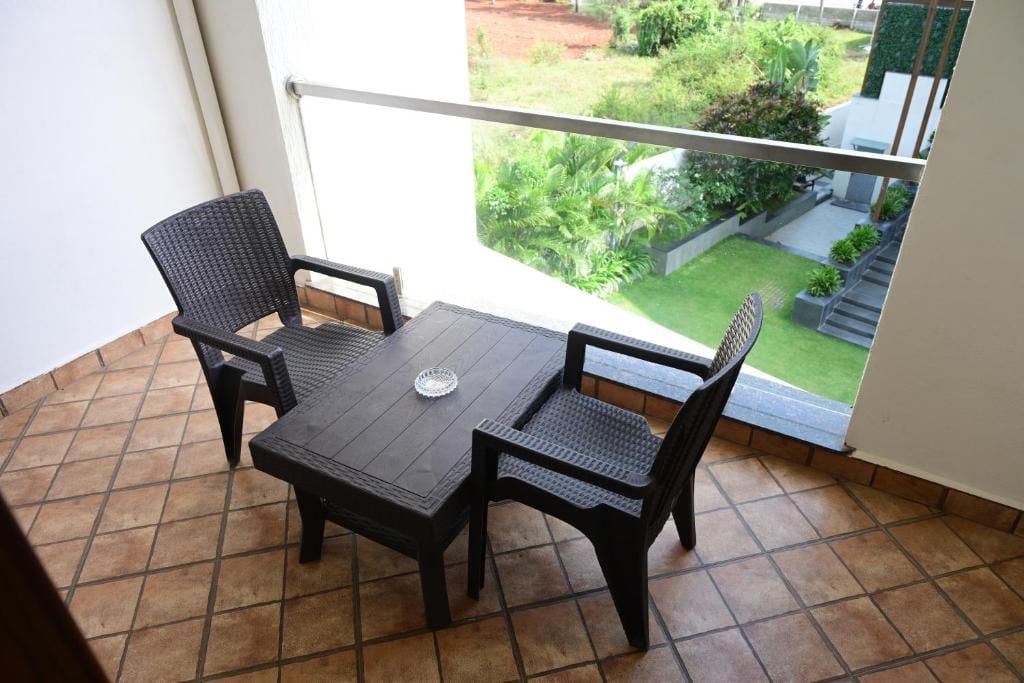 A balcony with a table and two chairs, a view of a garden, and a railing.