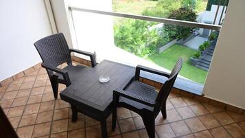 A balcony with a table and two chairs, a view of a garden, and a railing.