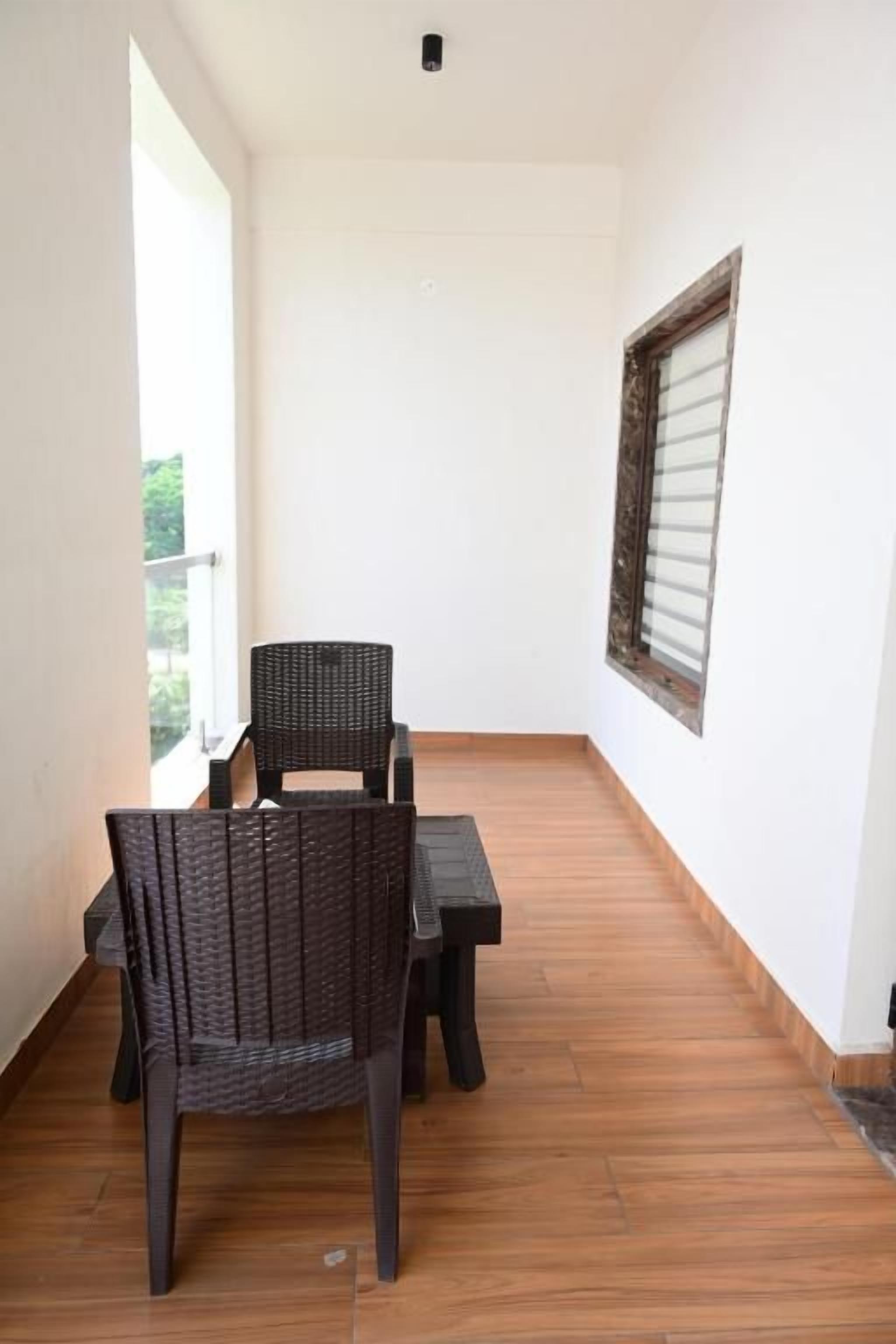 A balcony with a wicker chair and a small table, a window with blinds, and a wooden floor.