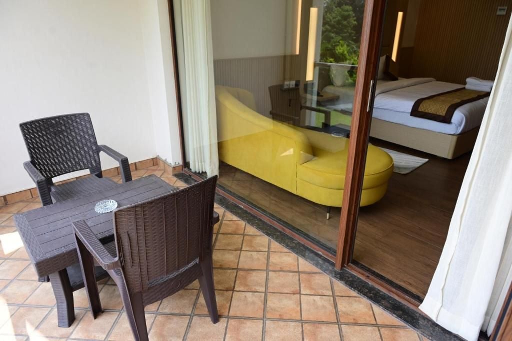 A balcony with a table and chairs, a yellow sofa, and a bed visible through a glass door.