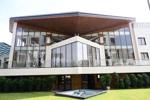 Un edificio moderno de dos pisos con grandes ventanales, techo plano y una piscina en el patio.