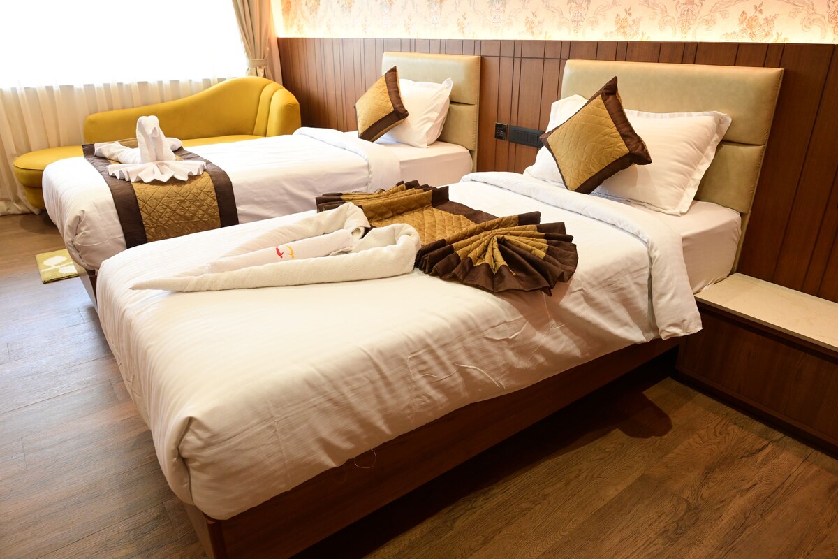 A hotel room with two beds, a yellow armchair, and a wooden headboard.
