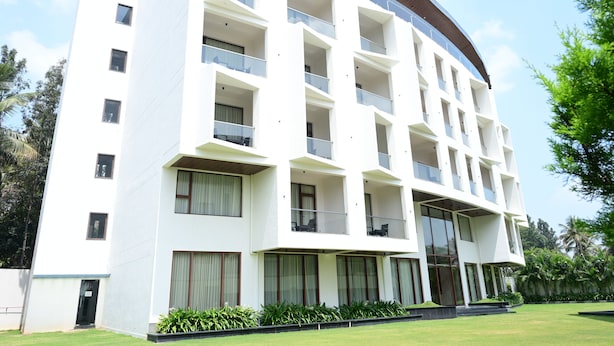 A multi-story hotel with balconies, large windows, and a flat roof. - IJ CROWNE (Mysore)