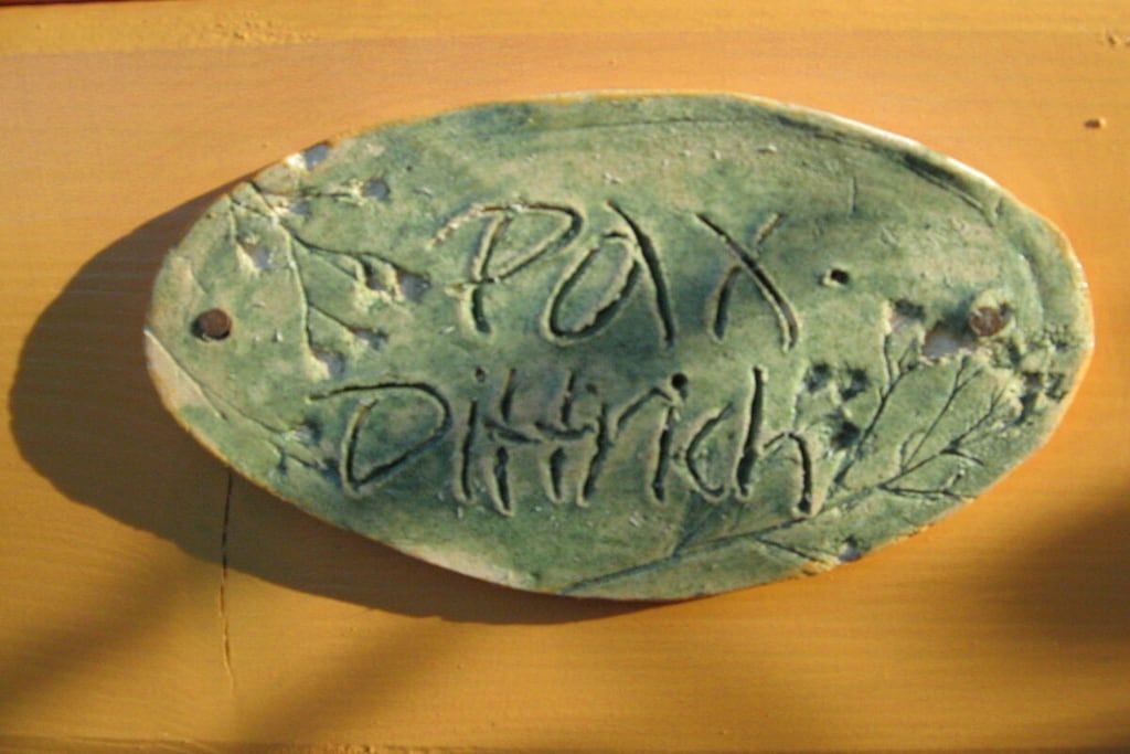 Un objeto verde en forma de óvalo con la inscripción 'PAX DIHINCH' sobre una superficie de madera.