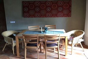Een eethoek met een ronde tafel, vier houten stoelen, een blauwe tafelkleed en een decoratieve wandhanger.