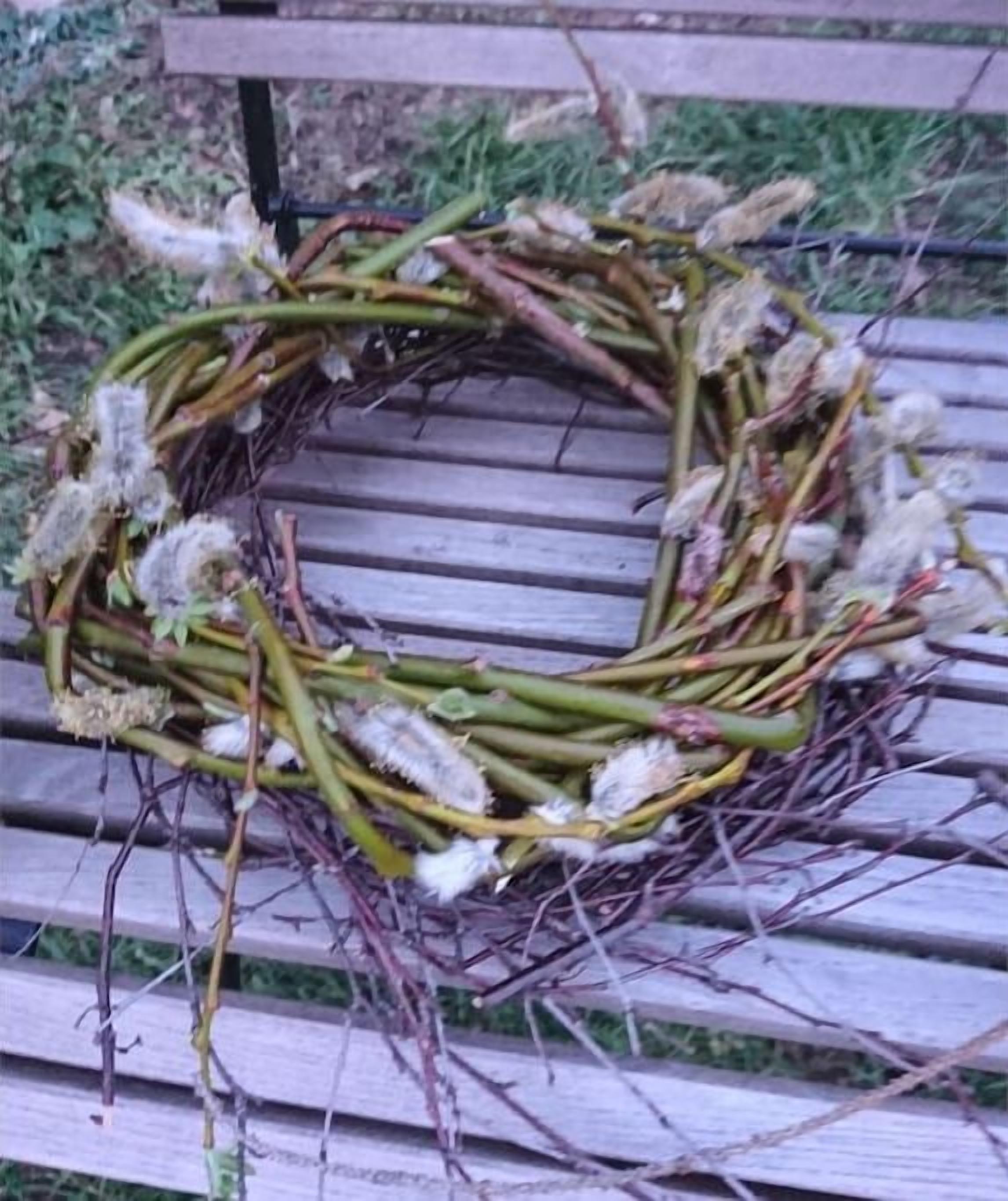 A wreath made of branches and dried flowers on a wooden bench.