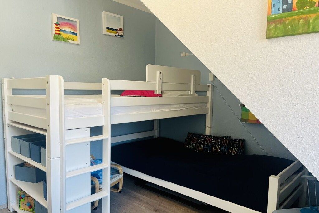 Un lit superposé avec des tiroirs de rangement et un bureau, une petite chaise, et un mur orné de deux tableaux encadrés.