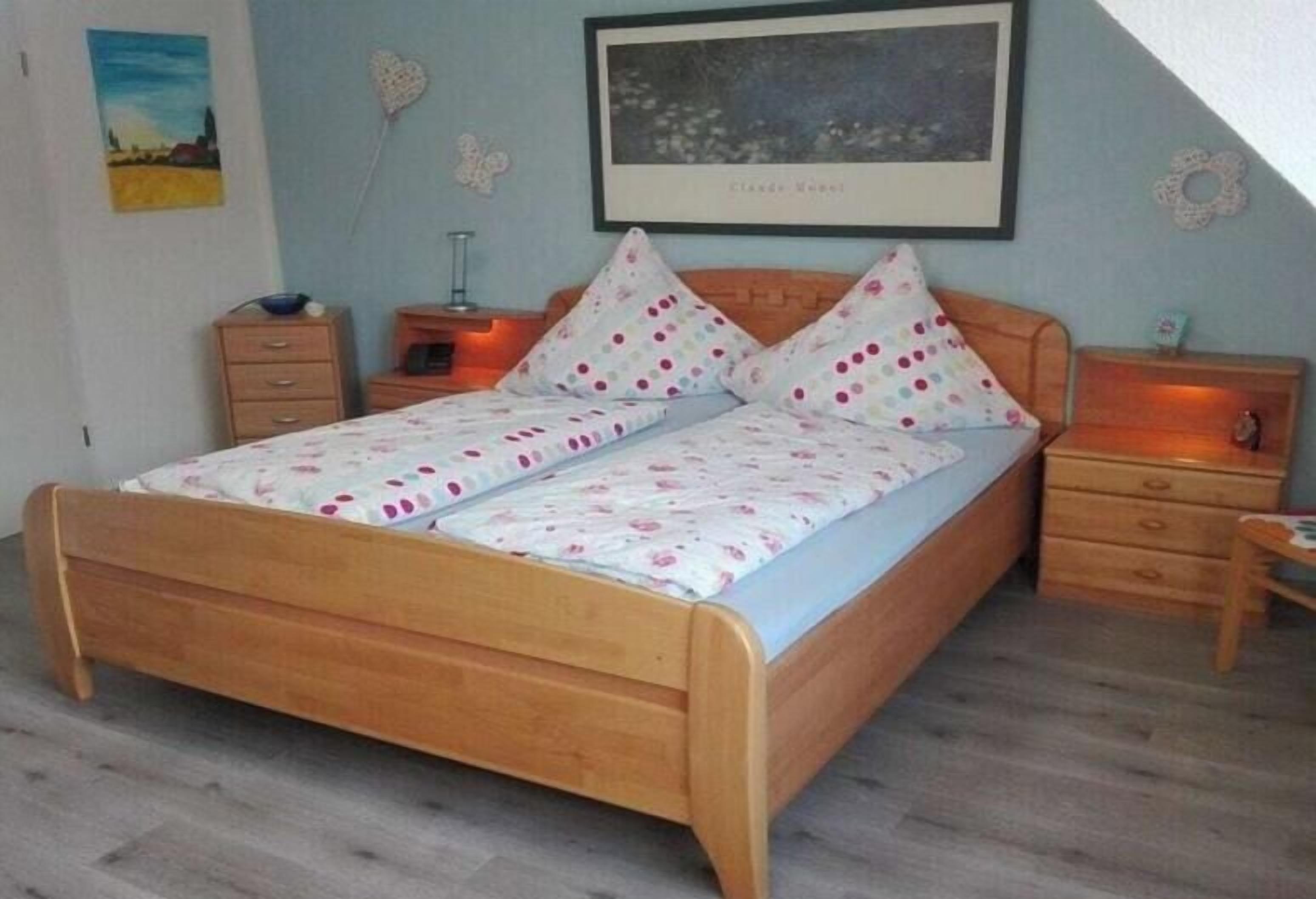 A bedroom with a wooden bed, two bedside tables, a nightstand, and a wall-mounted lamp.