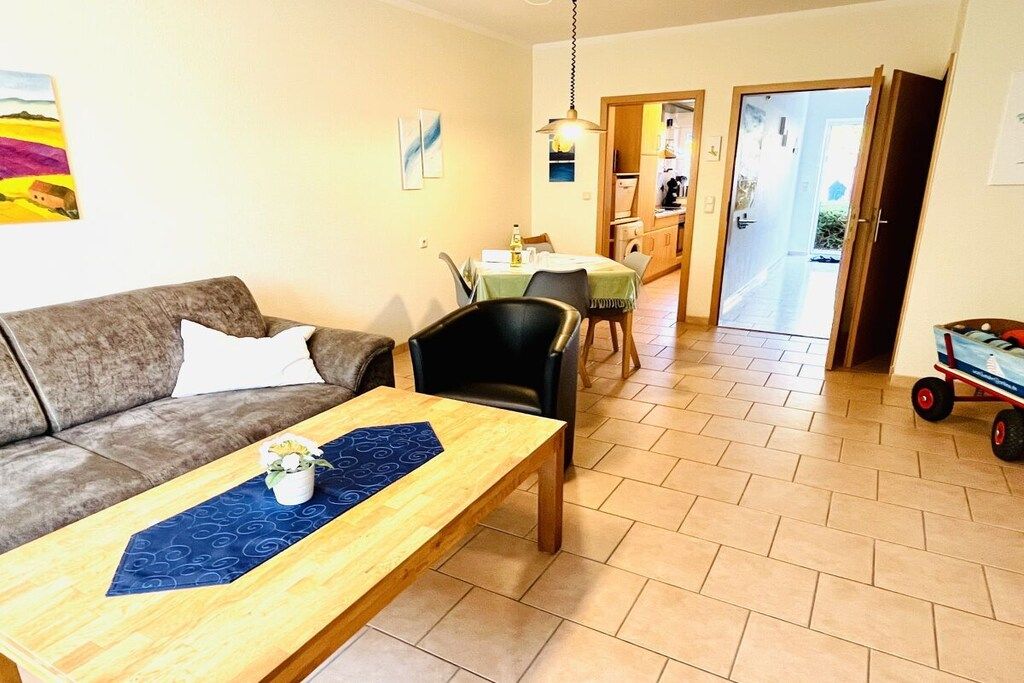 En stue med sofa, sofabord og spiseområde med stole og bord. Et køkken er synligt gennem en åben dør.