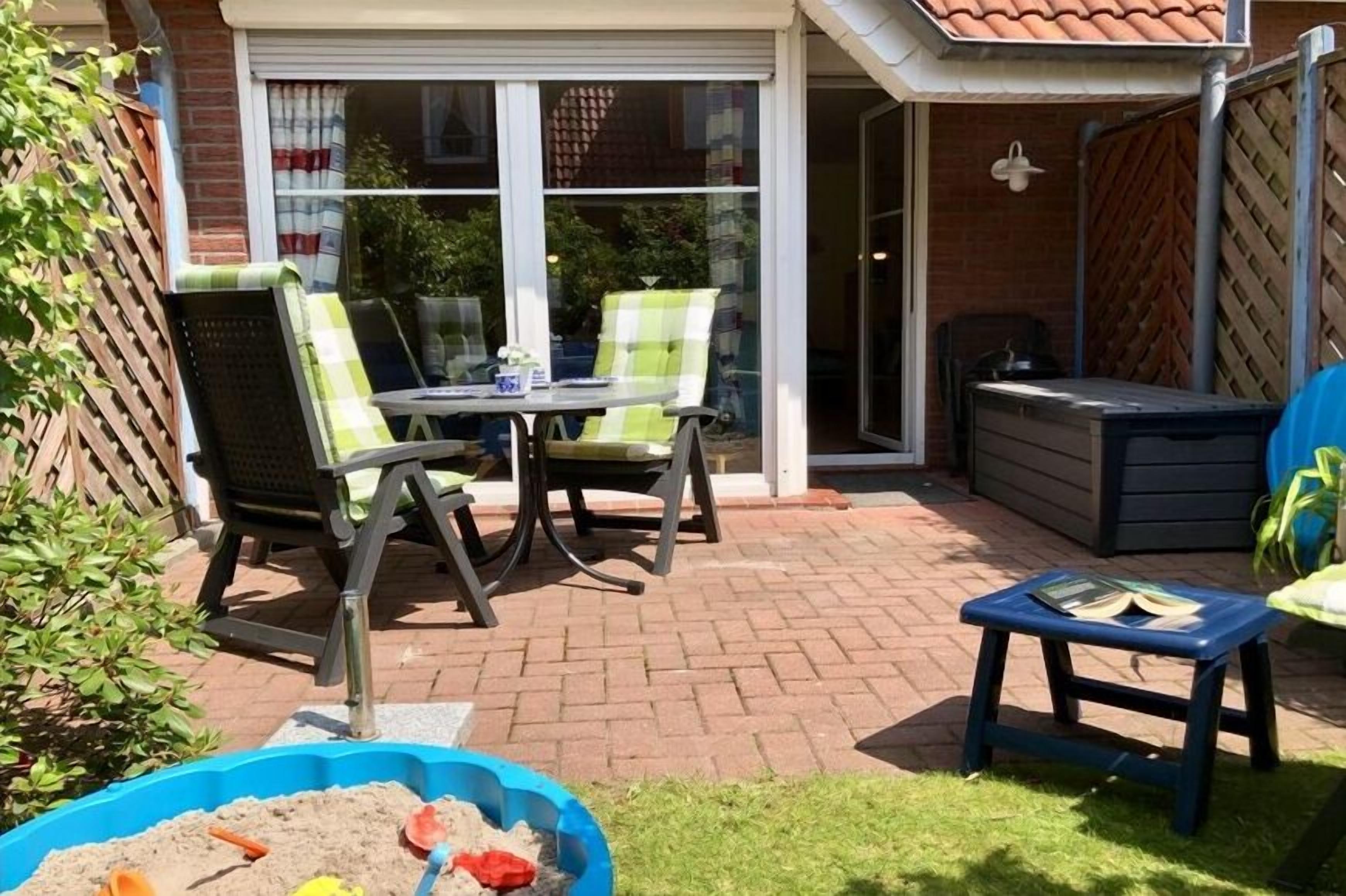 A patio with a table and chairs, a blue container with sand, and a small blue stool.