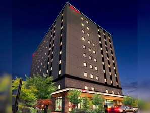 Et moderne hotel med et tydeligt 'Laient' skilt, flere etager og en bil i forgrunden.