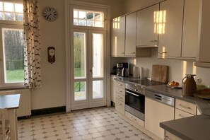 A kitchen with a double door leading to a garden, a clock on the wall, and a coffee maker on the counter. - Country house by Lake Ukleisee (Eutin-Sielbeck)