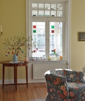Ein Zimmer mit Heizkörper, einem Fenster mit Blick auf die Straße und einem armchair mit Blumenmuster.